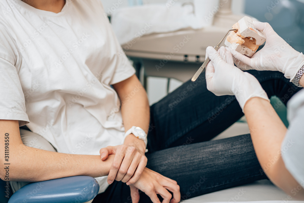cropped female dentist in medical gloves showing prosthesis to patient, give example of patient's teeth after treatment cropped female dentist in medical gloves showing prosthesis to patient, give example of patient's teeth after treatment