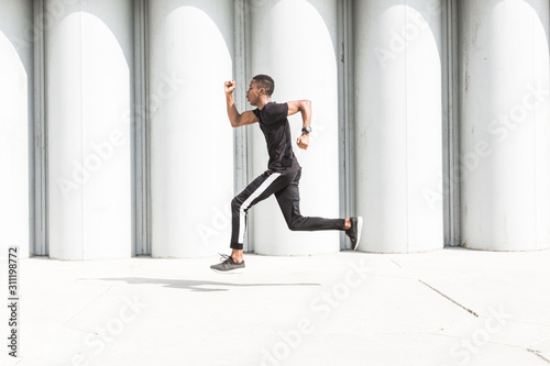 Athletic young afroamerican man running on the promenade. Black Male runner sprinting outdoors. Healthy lifestyle concept. © xartproduction