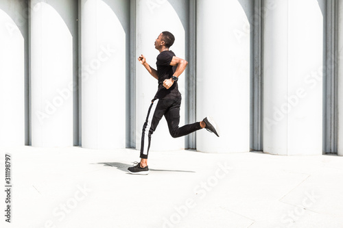 Athletic young afroamerican man running on the promenade. Black Male runner sprinting outdoors. Healthy lifestyle concept.