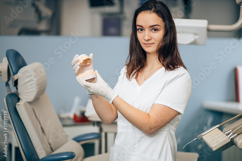 portrait of dental specialist at work, wearing white doctor's uniform, using medical instruments and equipment, holding prosthesis in hands. Healthcare concept