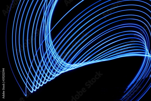 Long exposure photograph of neon blue colour in an abstract swirl, parallel lines pattern against a black background. Light painting photography.