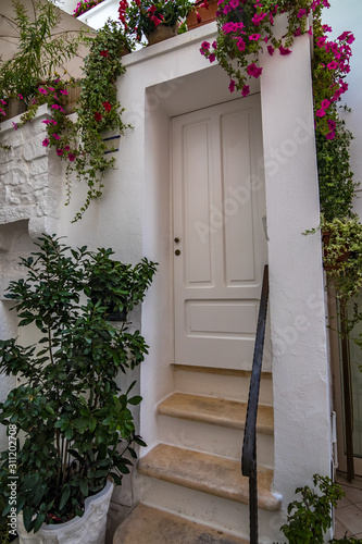Scenic sight, street view from the beautiful town of Locorotondo, Bari province, Apulia, Puglia , Southern Italy. Residential building whitewashed front facade with white wooden door and green plants.