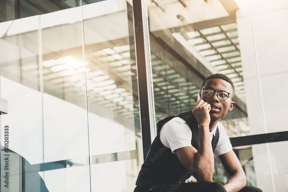 Young african american business man in suit and eyeglasses talking on the phone on the background of the business center Young african american business man in suit and eyeglasses talking on the phone on the background of the business center