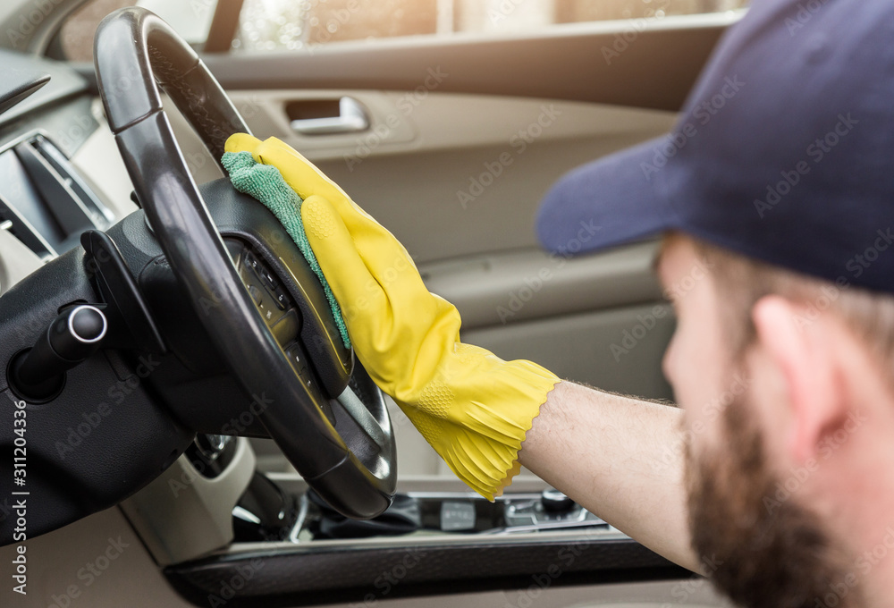 Cleaning service. Man in uniform and yellow gloves washes a car interior in a car wash