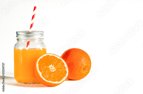 Glass jar with a tube with freshly squeezed orange juice stands on a white background next to fresh oranges photo