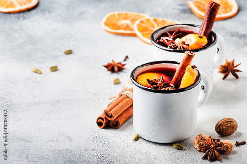 Mulled wine in white metal mugs with cinnamon, spices and orange on concrete background, traditional drink on winter holiday. Copy space for text photo