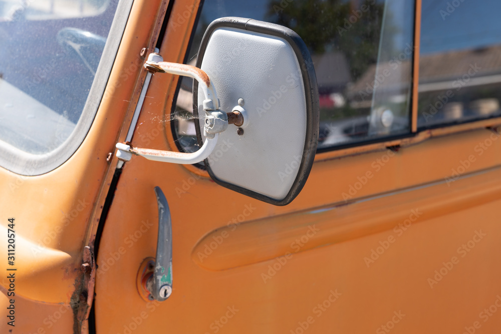 Side rear-view mirror and reflection in the window on orange retro vintage car