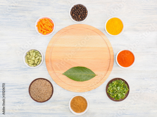 Round kitchen cutting board and ingredients for cooking: black pepper, turmeric, chili, green grass, masala, cumin (jeera), cardamom, carrot. Healthy eating concept