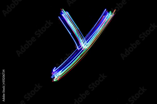 Long exposure photograph of a letter y in neon colour in an abstract swirl, parallel lines pattern against a black background. Light painting photography.