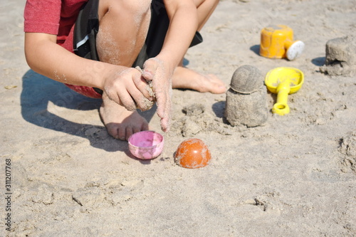 A child plays with molds in the sand. Beach holidays with children.