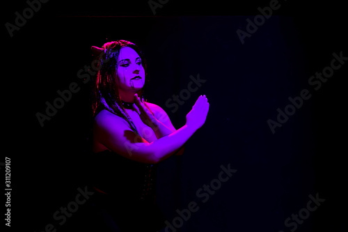 A woman in the guise of a devil dancing on a black background in purple lighting.
