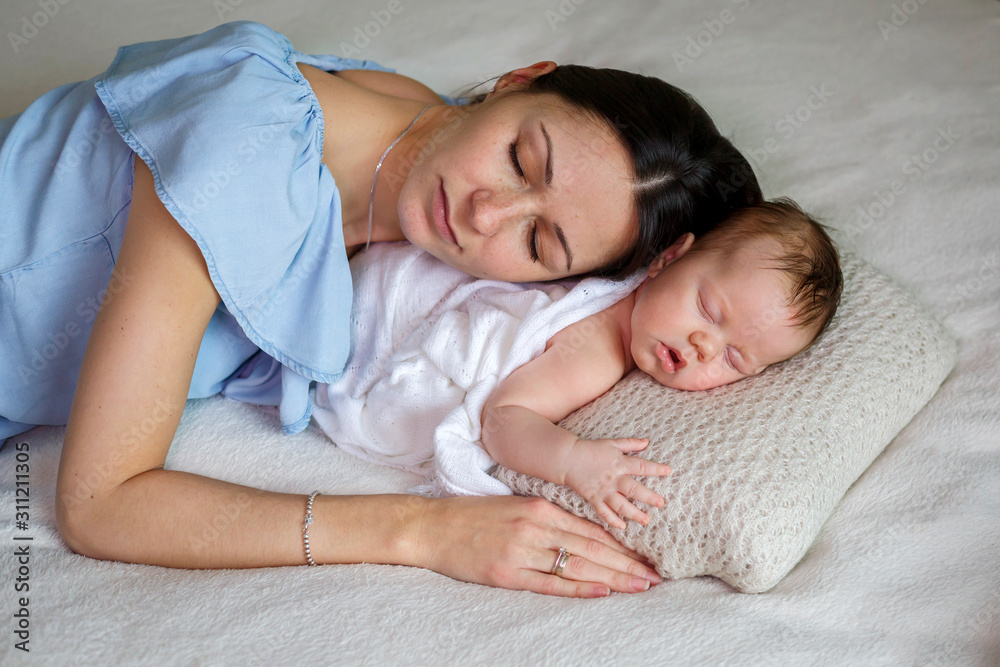 Young mother holding her sleeping newborn baby in her arms in light bedroom. Family, motherhood, love, health and care Young mother holding her sleeping newborn baby in her arms in light bedroom. Family, motherhood, love, health and care