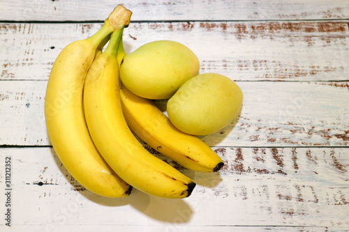 bunch of bananas and two ripe mangos on wooden table background