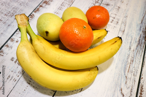 fresh fruits banana, yellow mango and mandarin on wooden table background