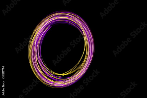 Long exposure photograph of neon pink and gold colour in an abstract swirl, parallel lines pattern against a black background. Light painting photography.