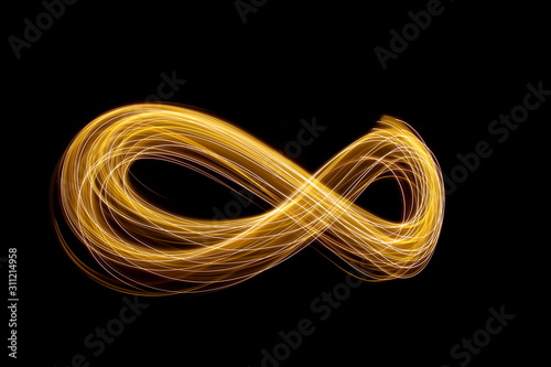 Long exposure photograph of an infinity loop in gold neon colour in an abstract swirl, parallel lines pattern against a black background. Light painting photography. photo