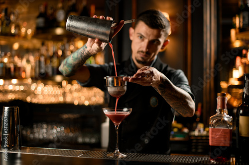 Bartender pouring cocktail from shaker through sieve