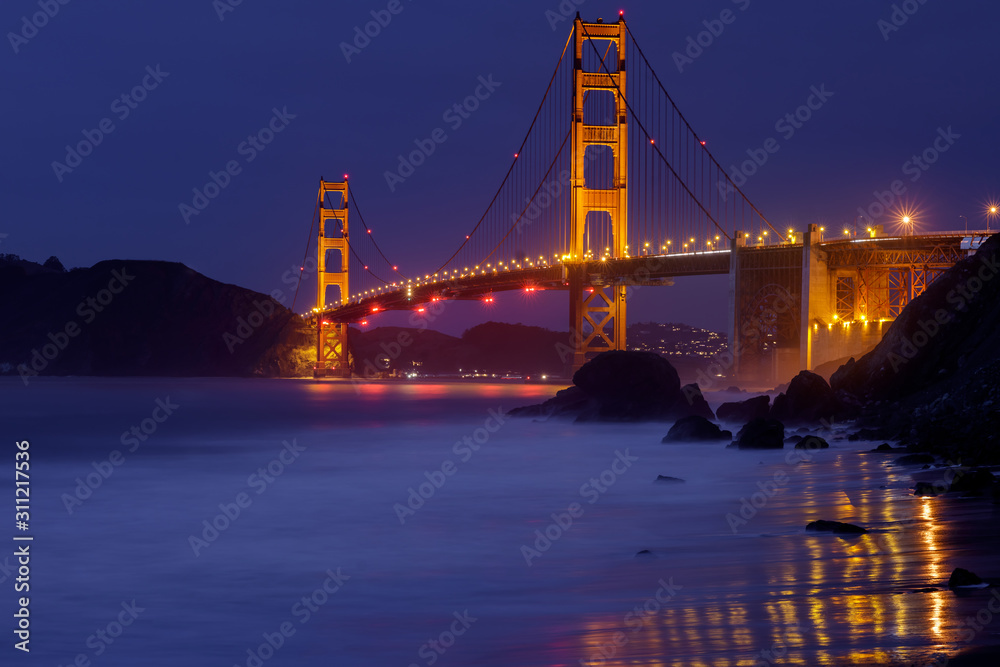 The Golden Gate Bridge glowing in the dark. Shot from Marshall Beach, San Francisco, California, USA. The Golden Gate Bridge glowing in the dark. Shot from Marshall Beach, San Francisco, California, USA.