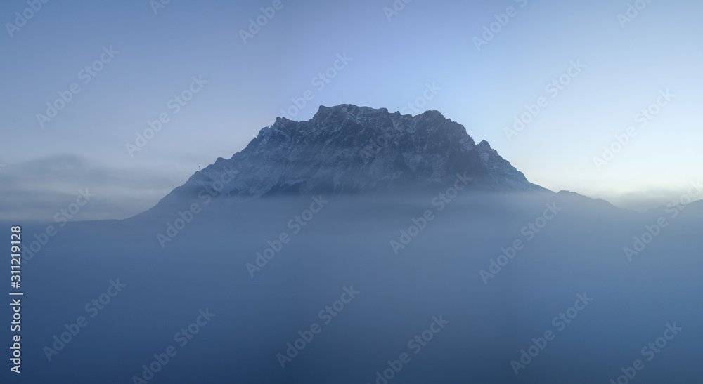 Zugspitze above the clouds and fog, mountain peak covered by snow, seen from Austria, Alps