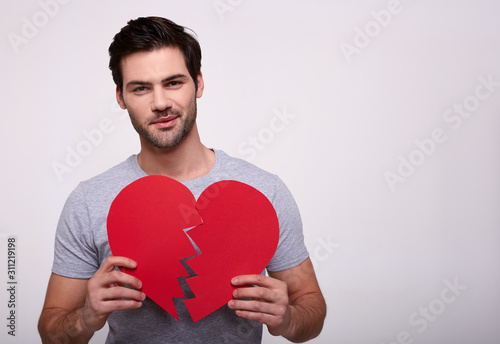 Portrait of a handsome young man with a broken heart in his hands.