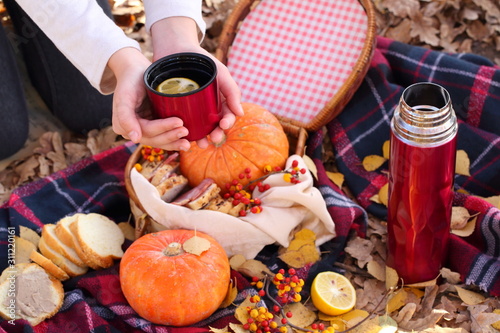 Children's hands hold a red mug with tea in the autumn park