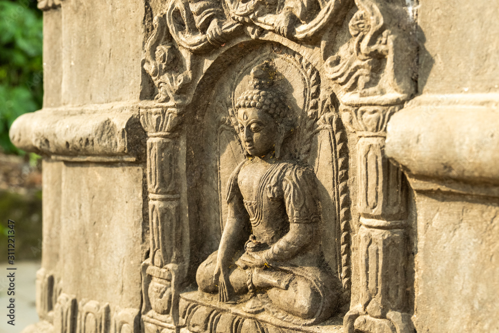 Ancient carved stone pillar with the image of a sitting Buddha and are decorated with traditional Buddhist patterns.