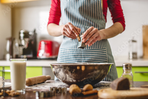 Cook housewife making cookies at home on a colorful kitchen. Woman rubbing on grater cinnamon to prepare the dough