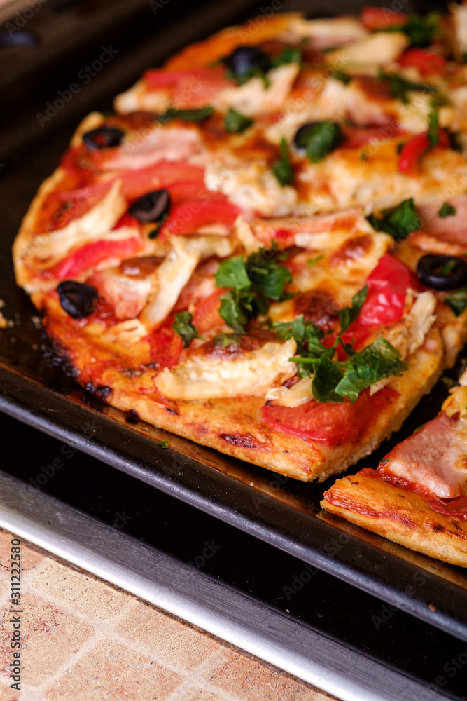 Fresh hot homemade pizza with chicken meat, ham, tomato, mozzarella cheese, black olives and parsley, angle view Fresh hot homemade pizza with chicken meat, ham, tomato, mozzarella cheese, black olives and parsley, angle view