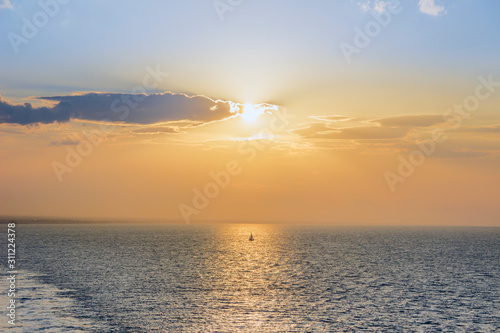 Sunset sailing. Seascape image with shiny sea and sailboat over cloudy sky and sun during sunset on Apulia coast  Italy.