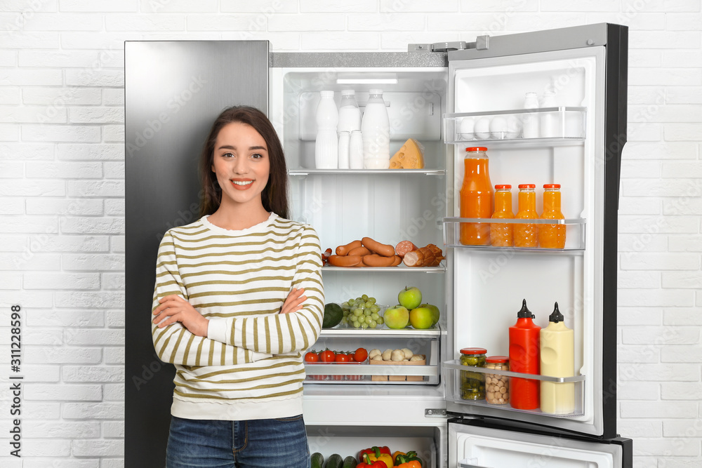 Happy young woman near open refrigerator indoors Happy young woman near open refrigerator indoors