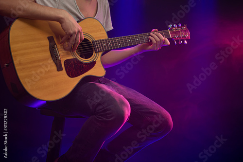 The musician plays an acoustic guitar. Beautiful background with colored light rays.