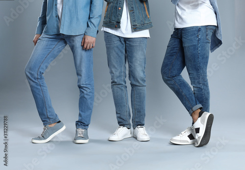 Group of young men in stylish jeans on grey background, closeup
