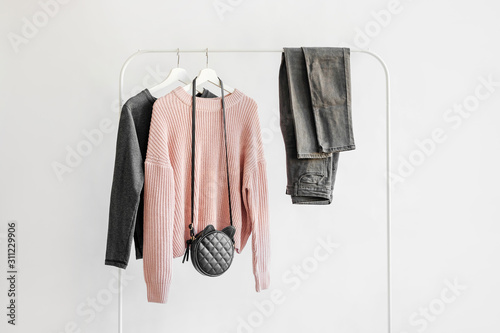 Female clothes in pastel pink and gray color on hanger on white background.  Jumper, shirt, jeans and bag. Spring/autumn outfit. Minimal concept. photo