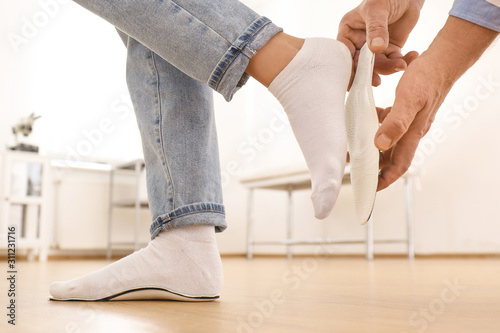 Male orthopedist fitting insole on patient's foot in clinic, closeup