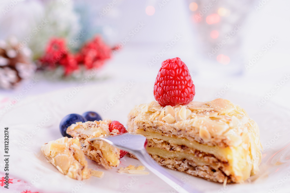 A portion of almond cake in a ceramic plate on the table next to Christmas decorations, close up A portion of almond cake in a ceramic plate on the table next to Christmas decorations, close up