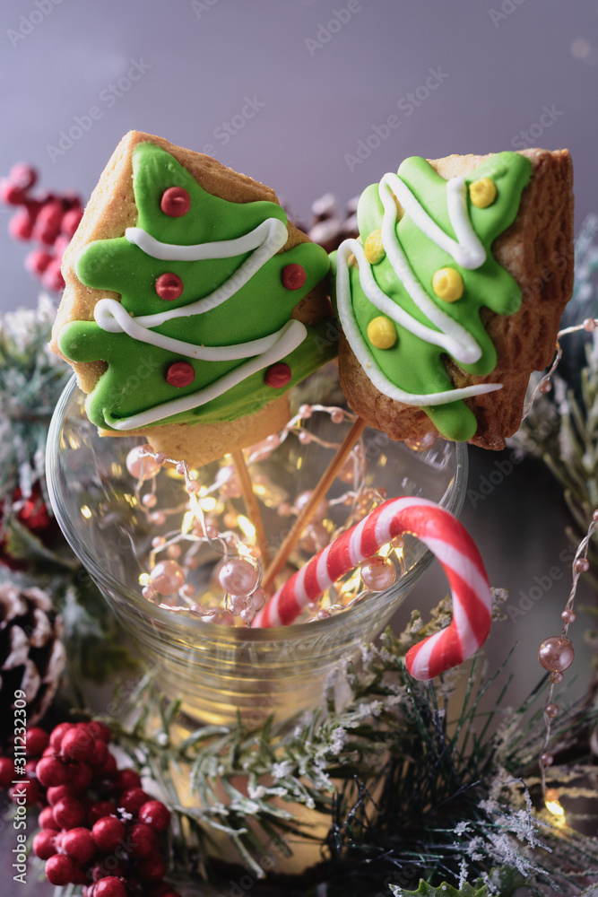Christmas tree-shaped gingerbread cookies and cane-shaped candy in a glass cup next to Christmas decorations