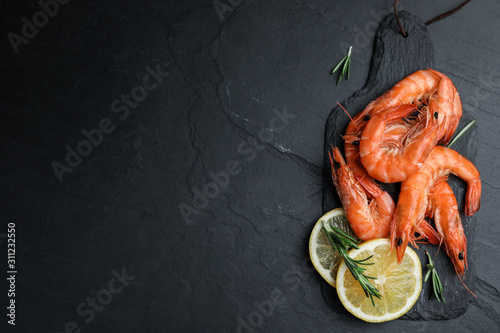 Delicious cooked shrimps with lemon and rosemary on black table, flat lay. Space for text photo