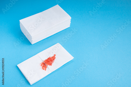 Blood on the hygiene napkin. Skincare mockup for design. Stack of disposable napkins on a blue background. Cosmetology concept. Bloody wound