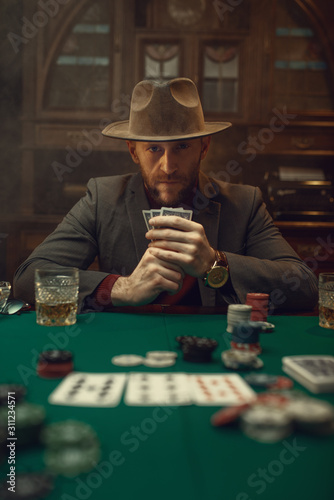 Poker player in suit and hat plays in casino