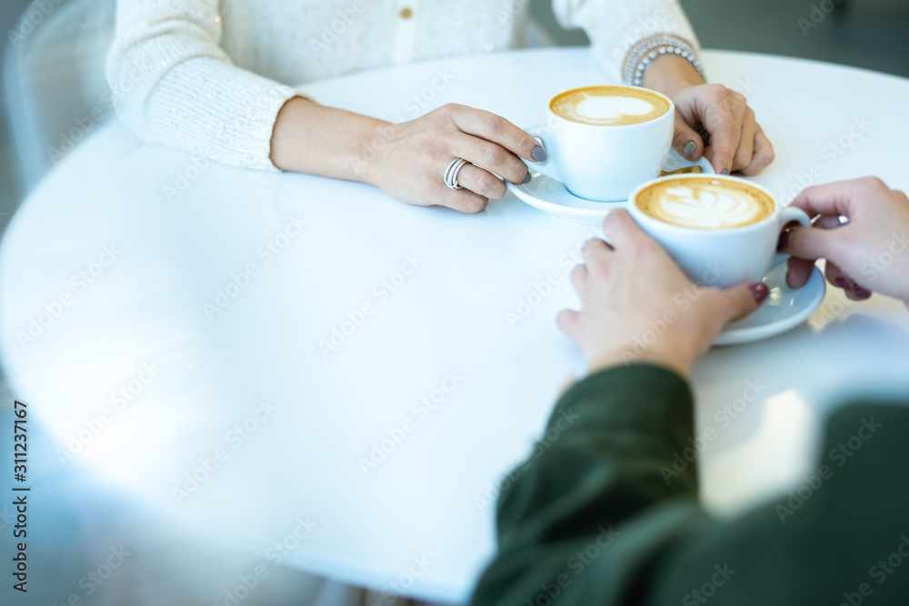 Hands of two young friendly women having cappuccino by table in cafe Hands of two young friendly women having cappuccino by table in cafe