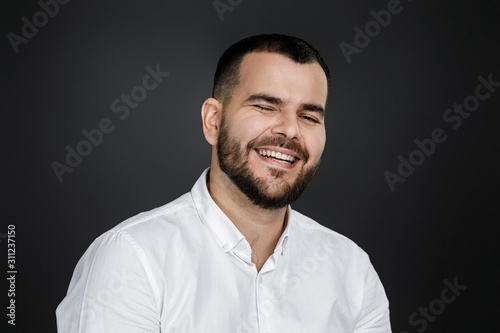 Close-up portrait of happy handsome bearded man laughing on black background
