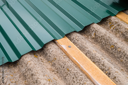 Repair of the old roof made of asbestos-cement sheets. Laying a metal profiled sheet with a fixing to wooden battens. photo