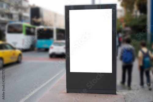 Blank white rectangular billboard at the roadside. On the left comes 2 teenagers on foot.