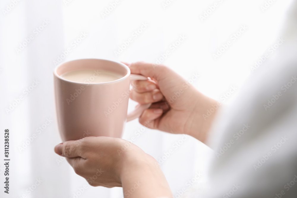 Woman with cup of hot drink near window at home in morning, closeup Woman with cup of hot drink near window at home in morning, closeup