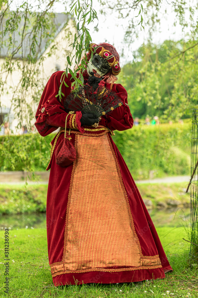 A woman acting in a venetian mask and red masquerade costume in a park