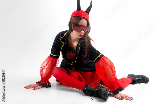 Sexy brunette girl in red tights, masquerade costume, futuristic glasses and devil horns on her head posing with passion over white background
