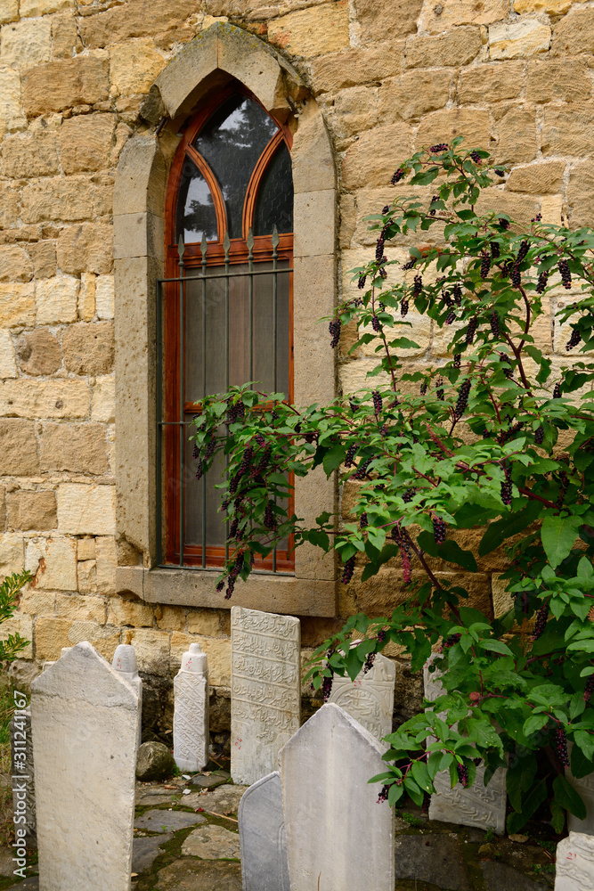 Φωτογραφία Mosque window with gravestones and pokeweed bush in hillside village of Yesilyur