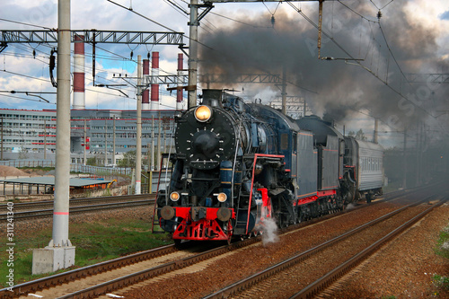 smoking steam train with a passenger carriage traveling by rail