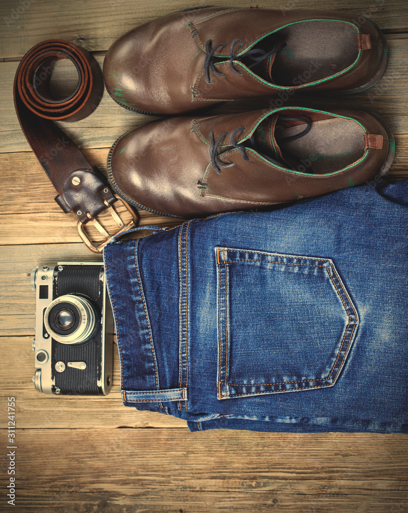 Still life with blue jeans, brown boots, leather belt and camera