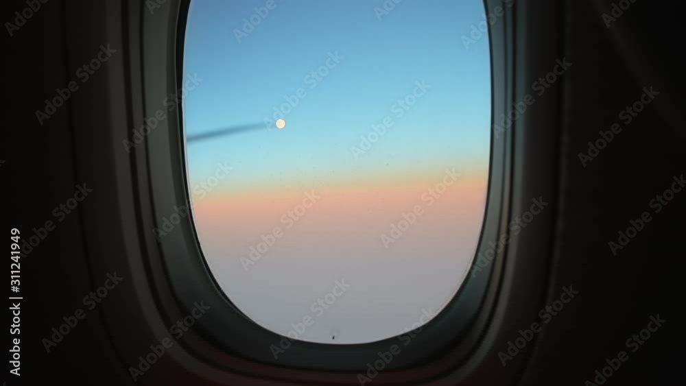 Hand closes airplane window to looks out during air travel. Passenger pov through plane window flight during sunset or sunrise. Close up of porthole of flying airplane at night. Aircraft above clouds. Hand closes airplane window to looks out during air travel. Passenger pov through plane window flight during sunset or sunrise. Close up of porthole of flying airplane at night. Aircraft above clouds.